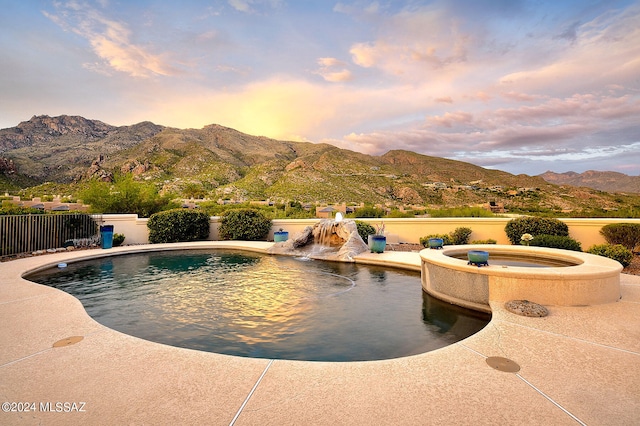 pool at dusk with an in ground hot tub and a mountain view