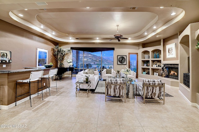 living room featuring built in features, light tile patterned floors, ceiling fan, a raised ceiling, and a mountain view