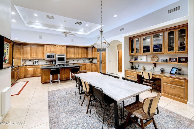 dining room featuring a tray ceiling, built in desk, ceiling fan, and light tile patterned flooring