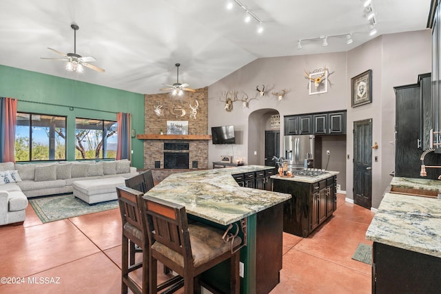 kitchen with stainless steel fridge, arched walkways, a kitchen island, open floor plan, and a sink