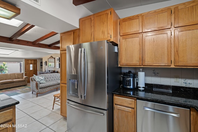 kitchen featuring beam ceiling, light tile patterned floors, tasteful backsplash, appliances with stainless steel finishes, and dark stone counters