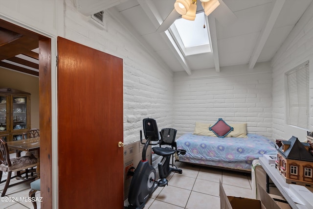 bedroom with light tile patterned floors, vaulted ceiling with skylight, ceiling fan, and brick wall