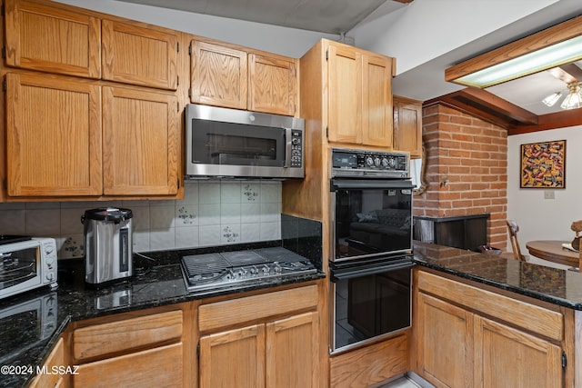 kitchen featuring vaulted ceiling, tasteful backsplash, gas stovetop, dark stone counters, and double oven