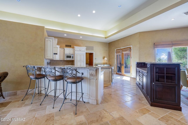 kitchen with kitchen peninsula, light stone countertops, stainless steel microwave, and a breakfast bar area