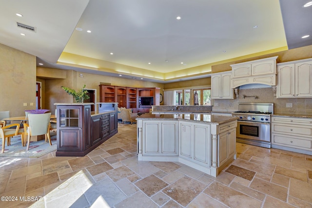 kitchen featuring kitchen peninsula, a center island, custom range hood, a tray ceiling, and high end stainless steel range