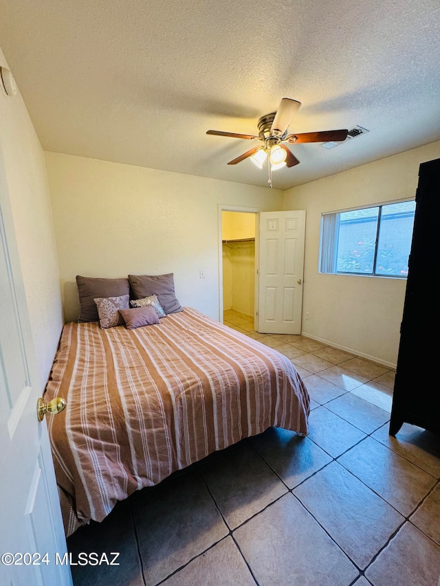 bedroom featuring ceiling fan, a textured ceiling, light tile patterned flooring, and a spacious closet