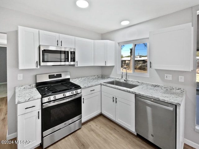 kitchen with appliances with stainless steel finishes, light wood-type flooring, white cabinetry, and sink