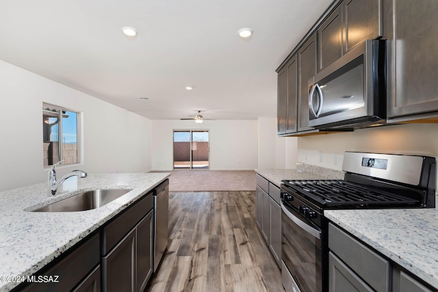 kitchen featuring ceiling fan, stainless steel appliances, hardwood / wood-style floors, sink, and light stone counters