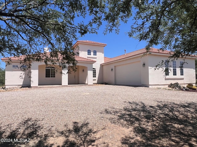 mediterranean / spanish-style house with gravel driveway, a tiled roof, stucco siding, and an attached garage