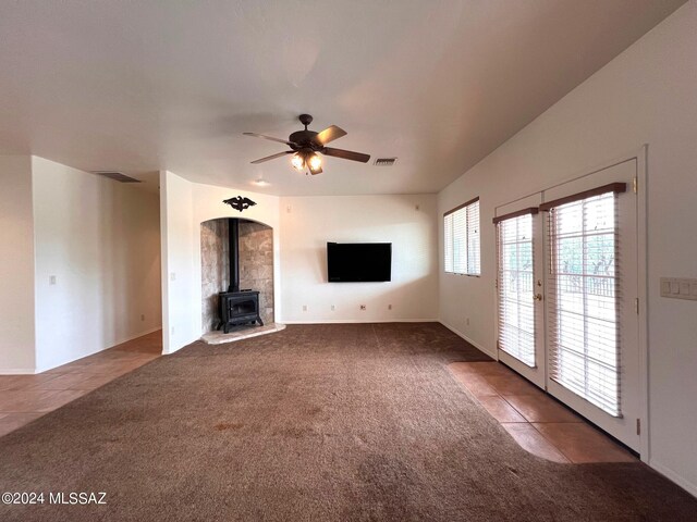 unfurnished living room with visible vents, a wood stove, carpet, and a ceiling fan