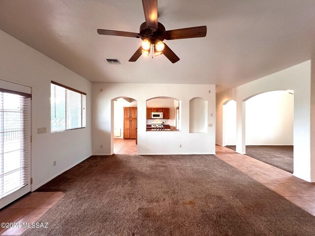 unfurnished living room with tile patterned flooring, carpet, arched walkways, visible vents, and a ceiling fan