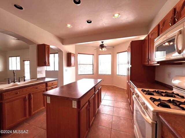 kitchen featuring a ceiling fan, a center island, white appliances, dark countertops, and arched walkways