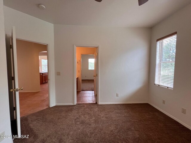 empty room with tile patterned floors, baseboards, arched walkways, ceiling fan, and carpet
