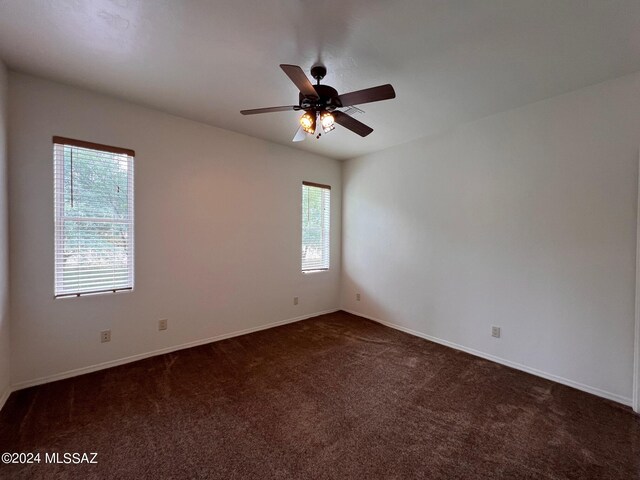 spare room with baseboards, dark colored carpet, and a ceiling fan