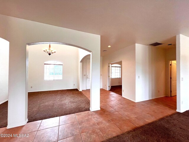 spare room with carpet flooring, visible vents, a chandelier, tile patterned floors, and arched walkways