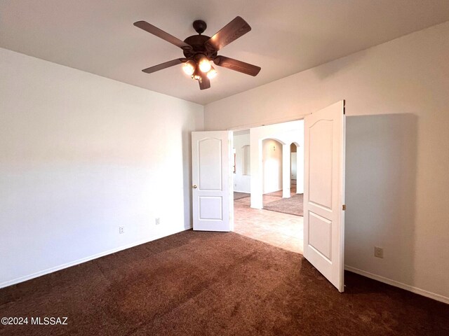 unfurnished bedroom with arched walkways, a ceiling fan, baseboards, and carpet