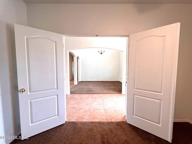 corridor featuring arched walkways, light tile patterned flooring, and light colored carpet