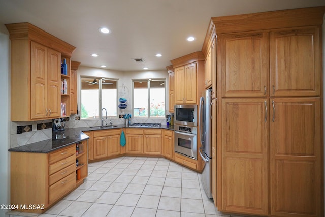 kitchen with sink, light tile patterned floors, appliances with stainless steel finishes, dark stone countertops, and backsplash