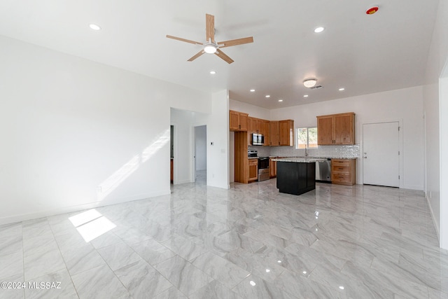 kitchen with ceiling fan, a kitchen island, a kitchen breakfast bar, decorative backsplash, and appliances with stainless steel finishes