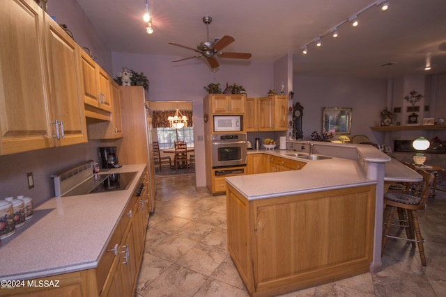 kitchen featuring stainless steel oven, ceiling fan with notable chandelier, sink, white microwave, and kitchen peninsula