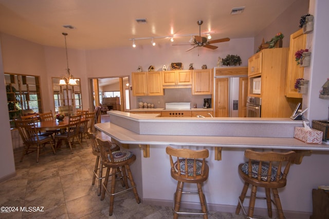 kitchen featuring a kitchen bar, built in appliances, pendant lighting, tile patterned flooring, and ceiling fan with notable chandelier