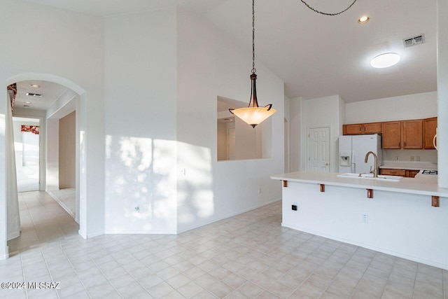 kitchen featuring white fridge with ice dispenser, sink, high vaulted ceiling, a kitchen breakfast bar, and pendant lighting