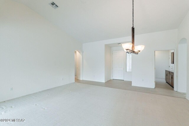 unfurnished living room featuring vaulted ceiling, light colored carpet, and an inviting chandelier