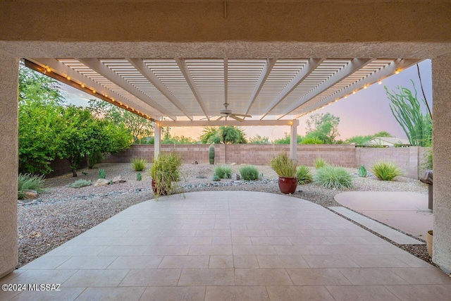 patio terrace at dusk featuring ceiling fan and a pergola