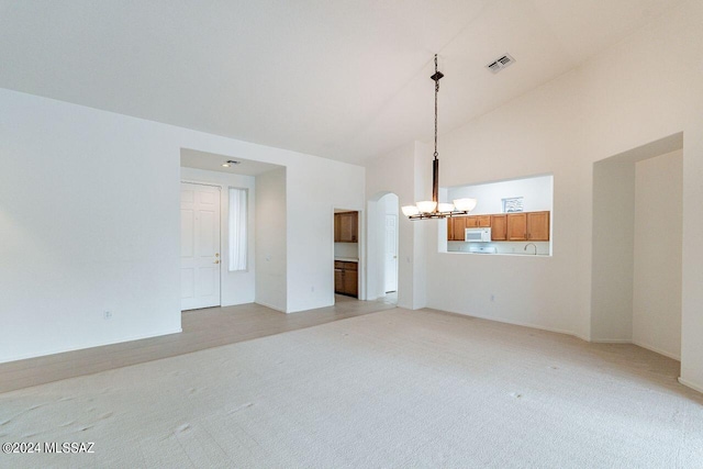 unfurnished living room with high vaulted ceiling, an inviting chandelier, and light colored carpet