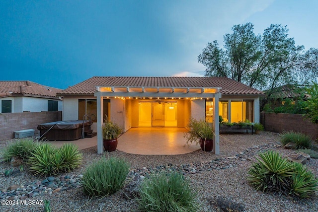 back house at dusk featuring a pergola, a hot tub, and a patio area