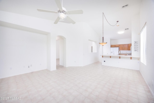 unfurnished living room featuring light floors, vaulted ceiling, arched walkways, and visible vents
