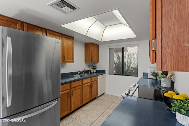 kitchen featuring sink, range, light tile patterned floors, stainless steel fridge, and white dishwasher