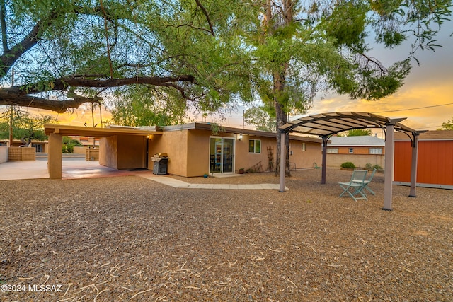 back house at dusk featuring a carport and a patio area