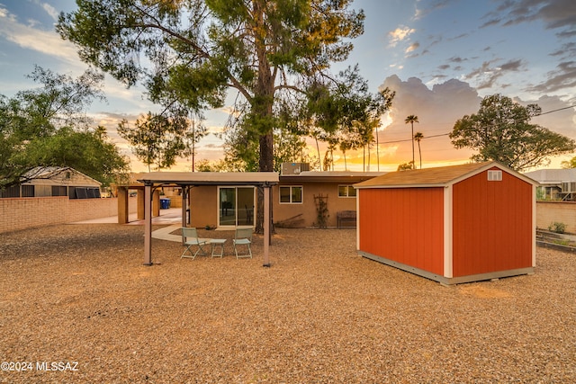 back house at dusk featuring a patio and a storage unit