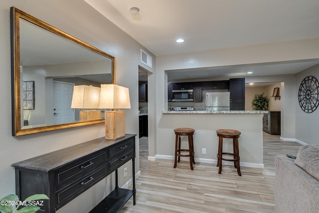 kitchen featuring appliances with stainless steel finishes, a kitchen bar, light wood-type flooring, and kitchen peninsula