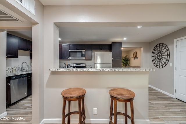 kitchen featuring light wood-type flooring, stainless steel appliances, a breakfast bar, and light stone counters