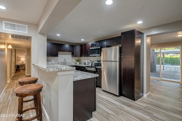 kitchen featuring a kitchen breakfast bar, appliances with stainless steel finishes, light stone countertops, sink, and dark brown cabinetry