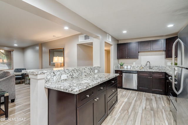 kitchen featuring appliances with stainless steel finishes, dark brown cabinets, and light wood-type flooring