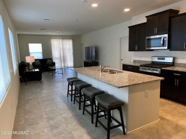 kitchen with sink, a breakfast bar, a kitchen island with sink, stainless steel appliances, and light stone counters