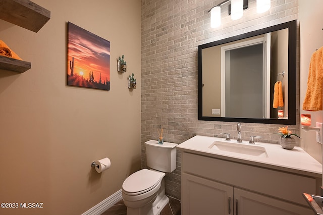 bathroom featuring vanity, toilet, baseboards, and brick wall