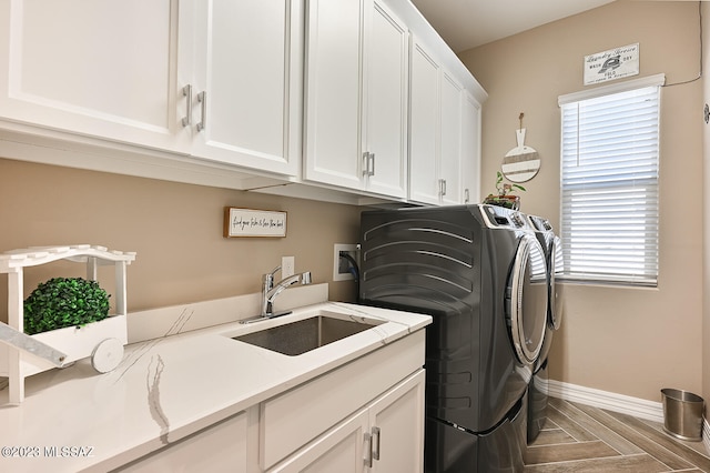 washroom with cabinet space, separate washer and dryer, baseboards, and a sink