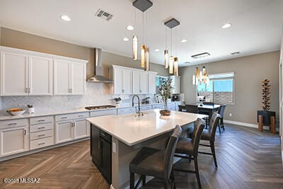 kitchen featuring backsplash, gas stovetop, light countertops, white cabinetry, and wall chimney exhaust hood