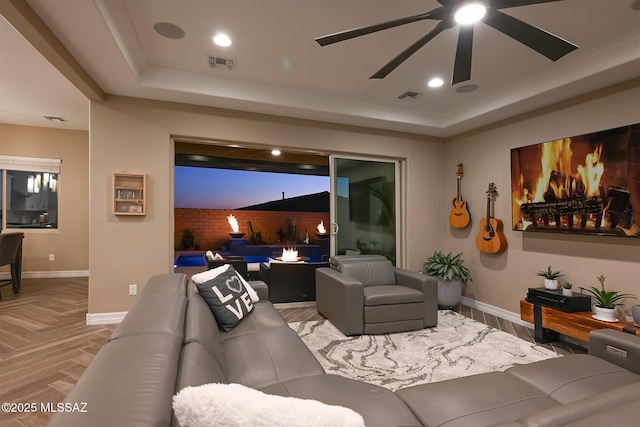 living area with visible vents, a raised ceiling, and baseboards