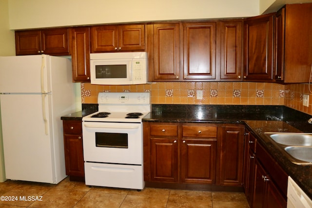 kitchen with light tile patterned floors, dark stone counters, white appliances, and sink