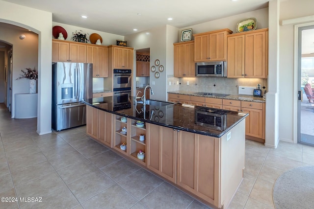 kitchen with sink, tasteful backsplash, a center island with sink, appliances with stainless steel finishes, and dark stone counters