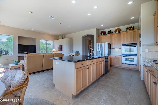 kitchen featuring sink, appliances with stainless steel finishes, backsplash, an island with sink, and light brown cabinetry