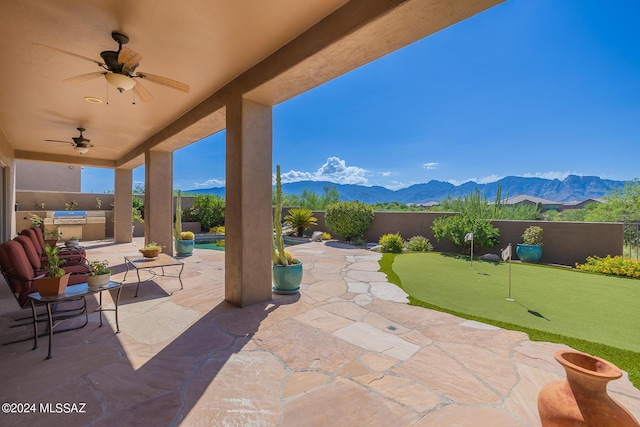 view of patio featuring exterior kitchen, a mountain view, a fenced in pool, and ceiling fan