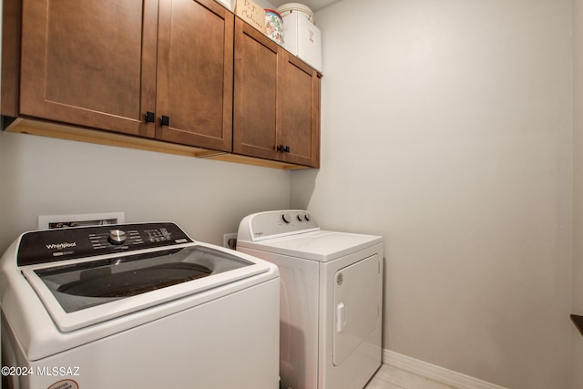 washroom with light tile patterned flooring, washing machine and dryer, and cabinets