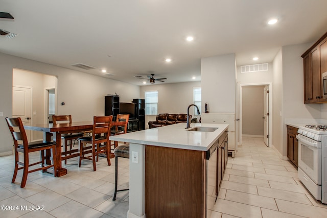 kitchen featuring light tile patterned flooring, white gas range, an island with sink, ceiling fan, and sink