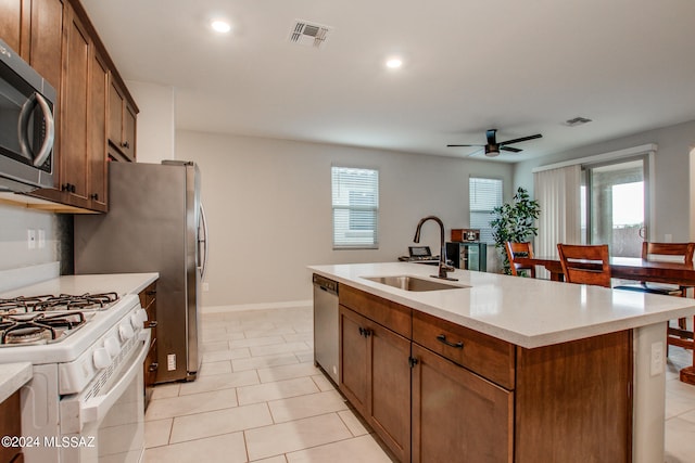 kitchen with stainless steel appliances, sink, light tile patterned floors, a kitchen island with sink, and ceiling fan